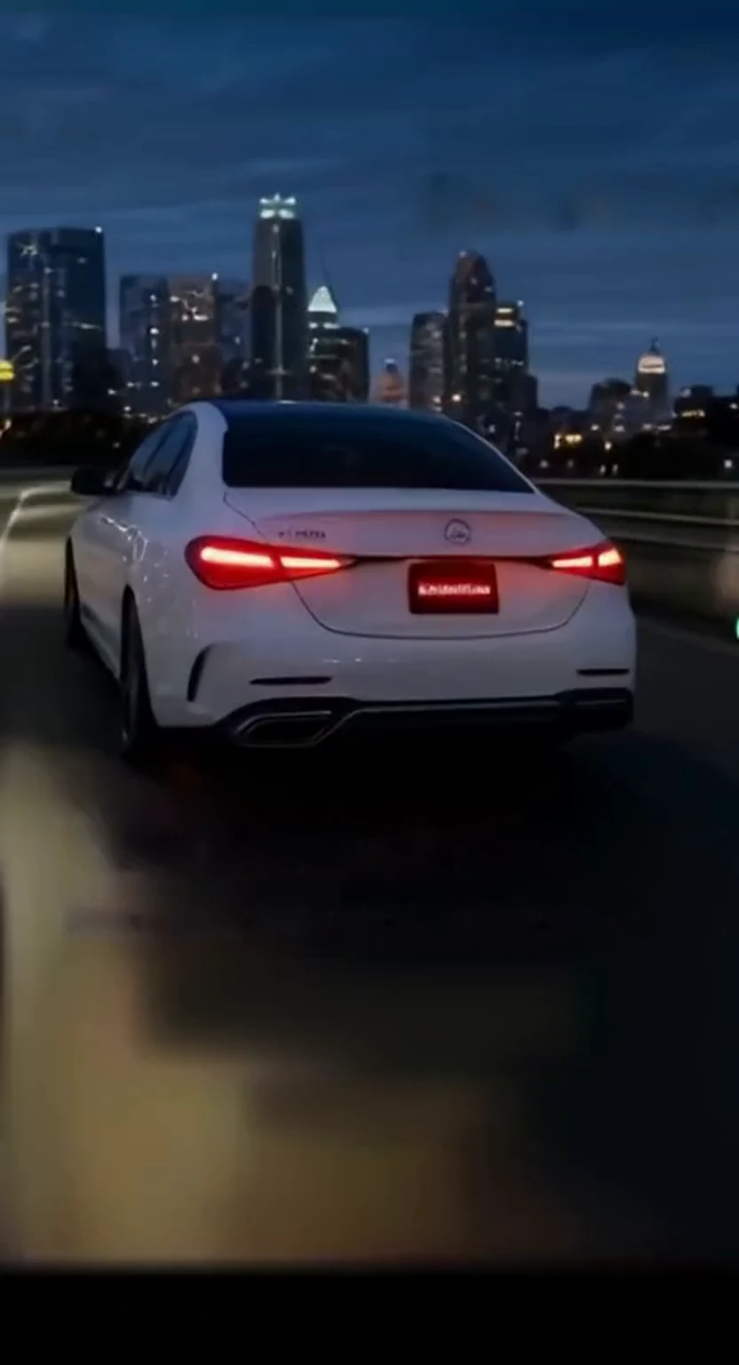 White sedan driving toward a nighttime city skyline
